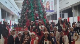 Personas vistiendo motivos navideños junto al árbol de navidad en el Centro Comercial Metrosol Maracaibo